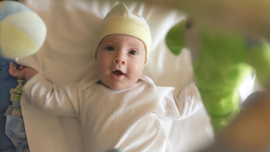 Baby liegt fröhlich unter einem Mobile.