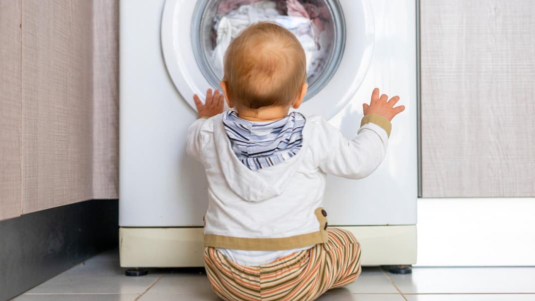 Baby sitzt vor der Waschmaschine und schaut hinein.