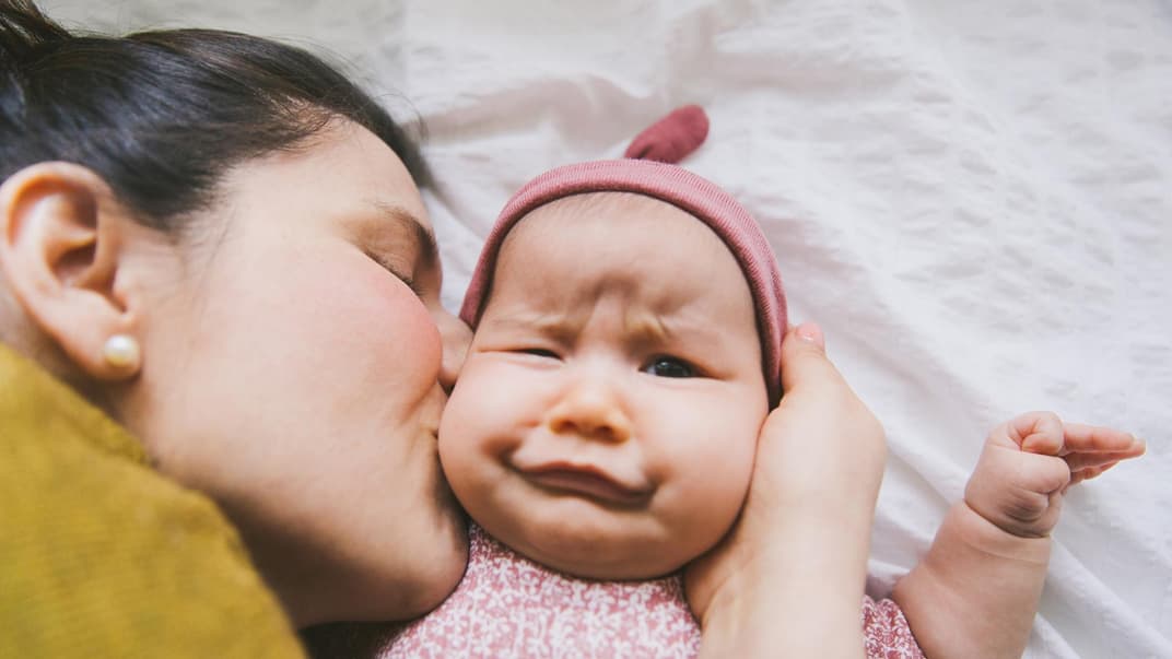 Ein Baby wird von seiner Mama geküsst und verdreht dabei die Augen. 