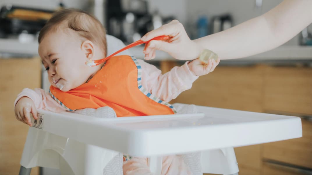 Ein Baby, das mit Brei gefüttert werden soll, dreht seinen Kopf weg.