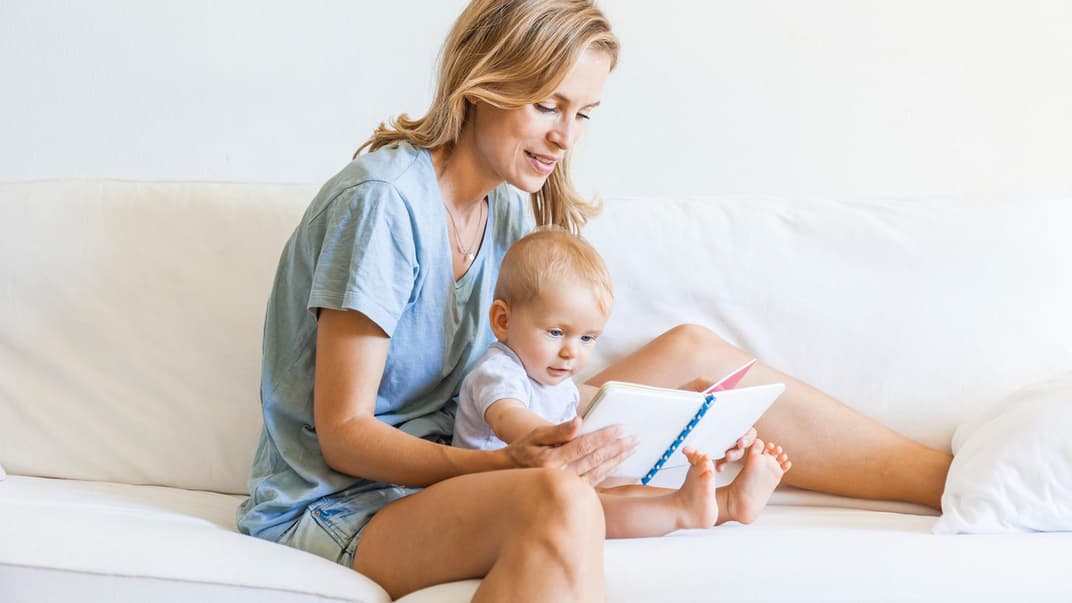 Mutter schaut Buch mit Baby an.