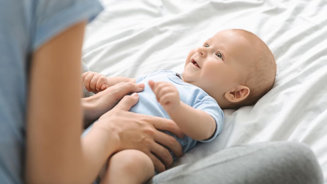 Mama hält Bäuchlein eines fröhlichen Babys.