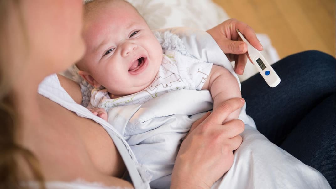 Eine Mutter misst bei ihrem weinenden Baby mit einem Fieberthermometer die Temperatur.