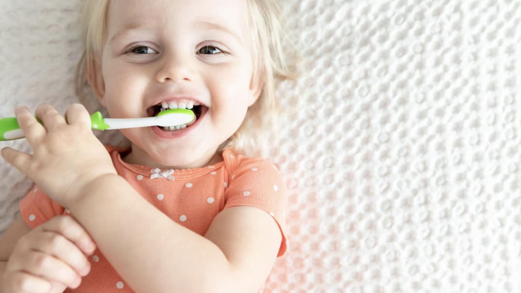 Kleines Mädchen kaut auf einer Zahnbürste.