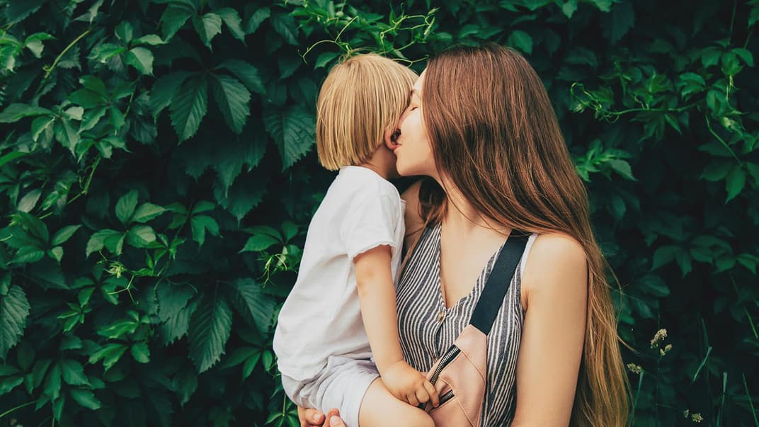 Mama küsst Ohr ihres Kindes.