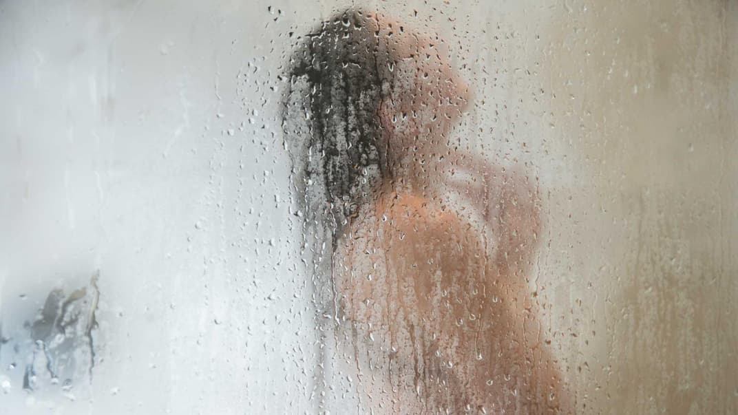 Frau hinter nasser Duschscheibe.