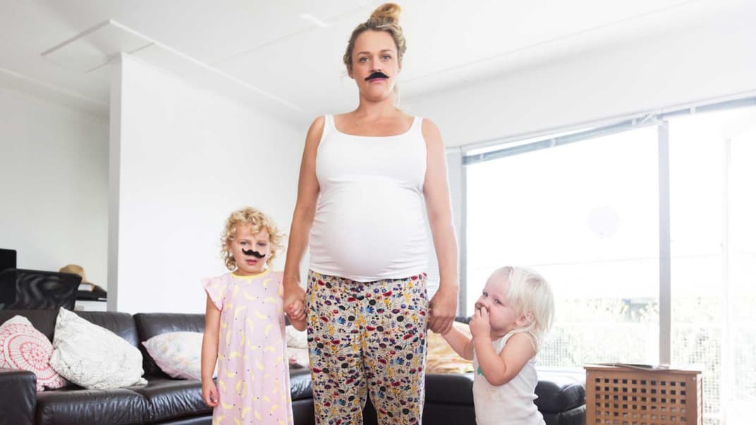 Schwangere Mutter mit zwei kleinen Kindern hat sich einen Schnurrbart aufgeklebt.