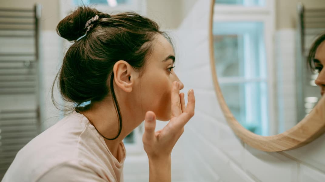 Eine Mutter tupft sich vor dem Spiegel eine Creme unter die Augen.
