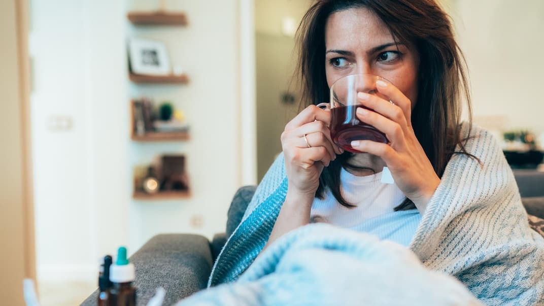 In Decke gehüllte Frau trinkt einen Tee.