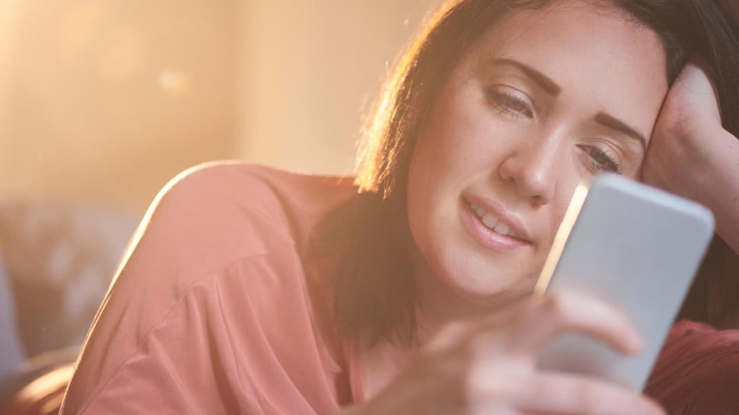 Frau lächelt, während sie auf ihr Smartphone schaut.