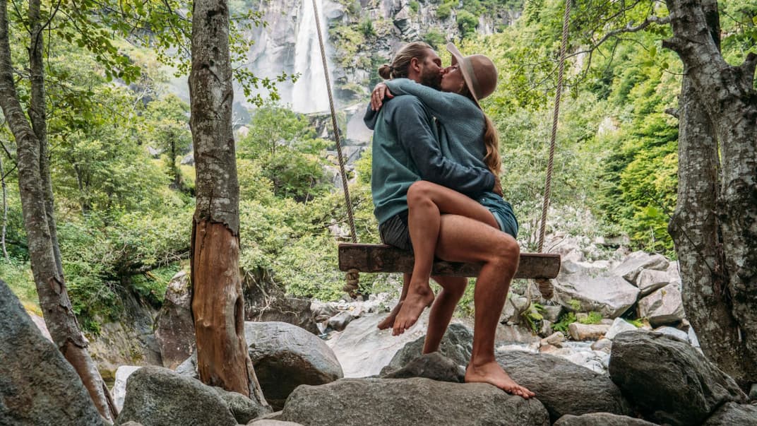 Paar sitzt sich küssend auf einer Schaukel in der Natur.