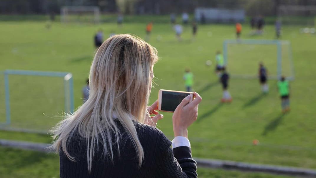 Mutter macht mit dem Smartphone Fotos vom Fußballspiel des Nachwuchses.