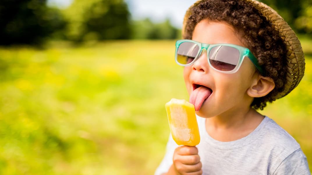 Ein Junge leckt an einem Eis aus Fruchtsaft. 