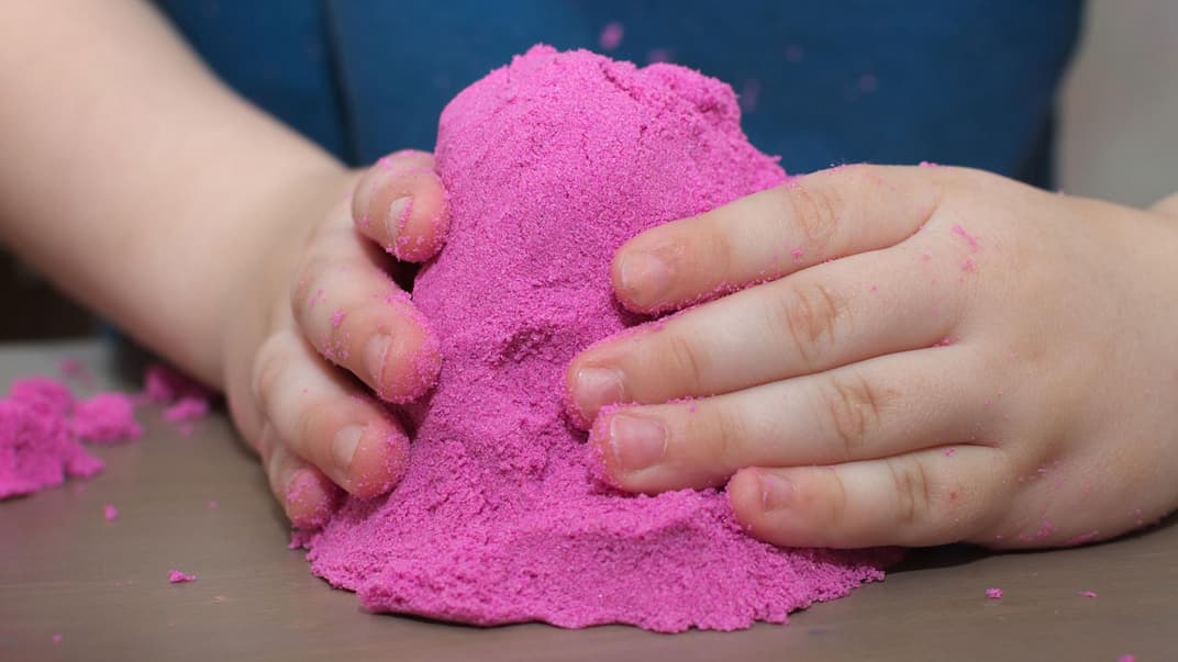 Kinderhände mit pinkfarbenem Kinetic Sand.