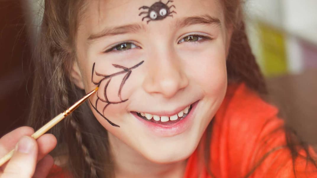 Mädchen mit geschminktem Spinnennetz auf der Wange und einer Spinne auf der Stirn.