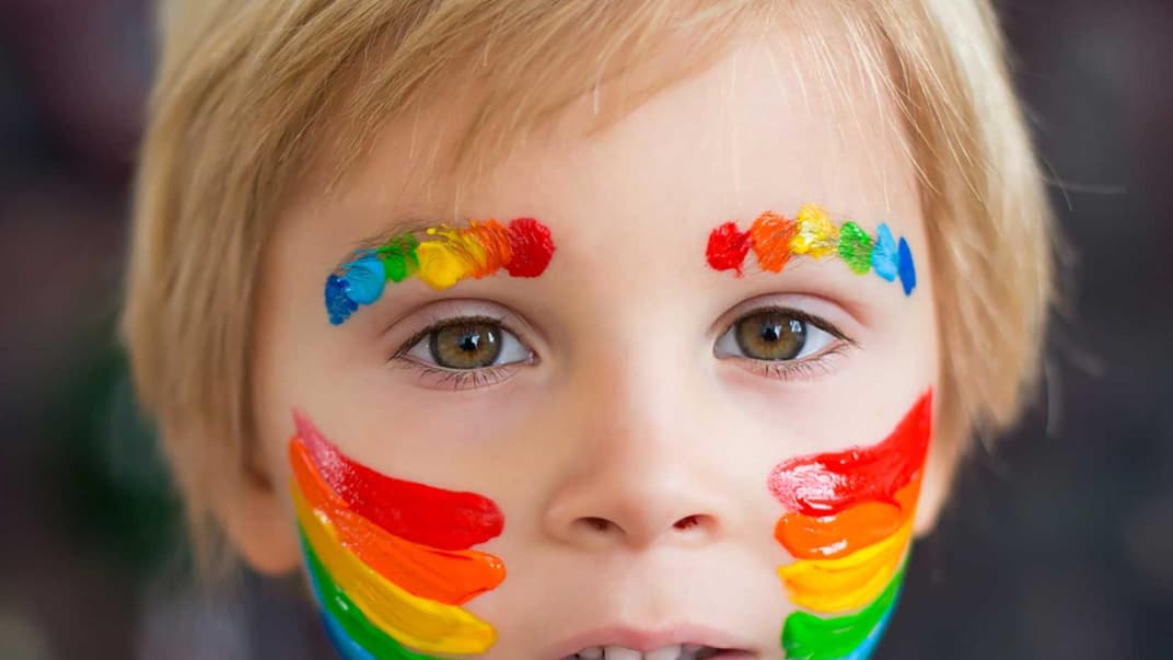 Junge mit geschminktem Regenbogen auf Wangen und Augenbrauen