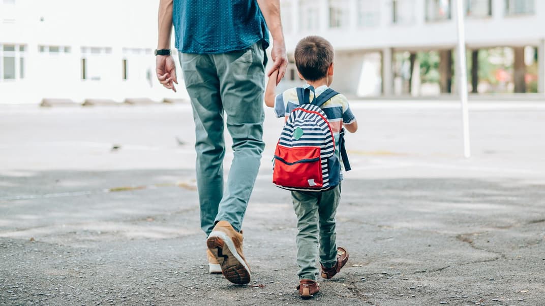 Vater geht mit kleinem Kind an der Hand zur Schule.