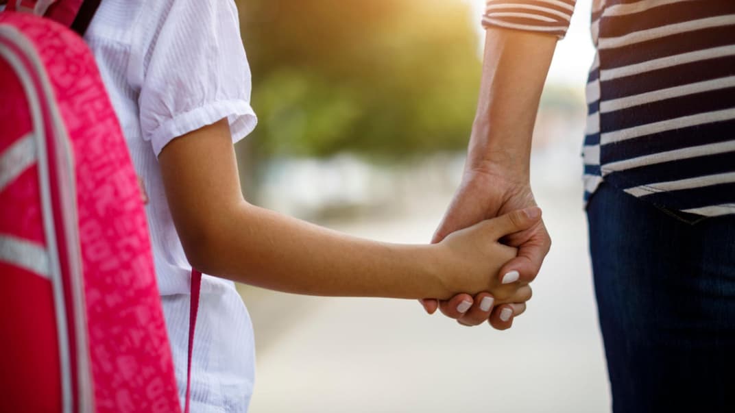 Schulkind an der Hand der Mutter.