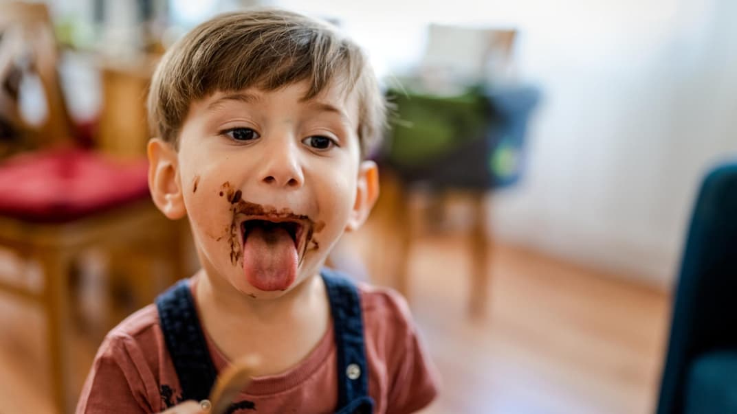 Kind streckt mit Schoko-verschmiertem Gesicht die Zunge raus.