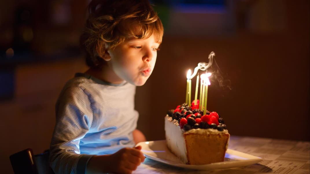 Rituale stärken Kinder.  Kind pustet Kerzen auf Geburtstagskuchen aus.