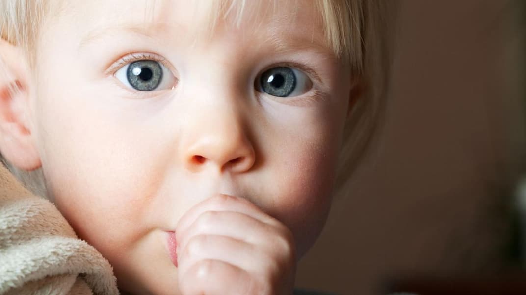Kleines Kind nuckelt mit großen Augen am Daumen.
