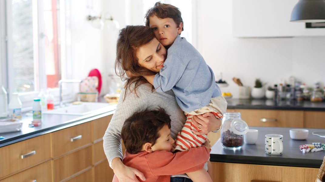 Mutter kuschelt in der Küche mit ihren beiden Kindern.