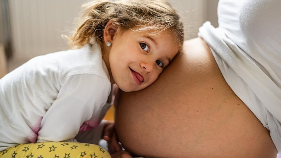 Fröhliches Mädchen lauscht am Babybauch.