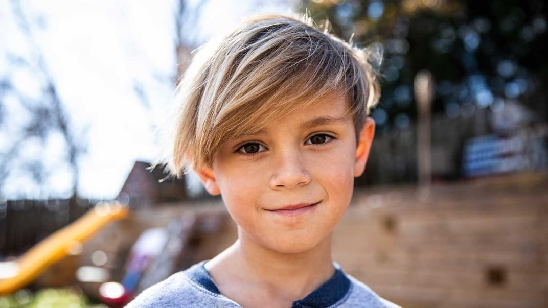 Blonder Junge mit längeren Haaren lächelt.