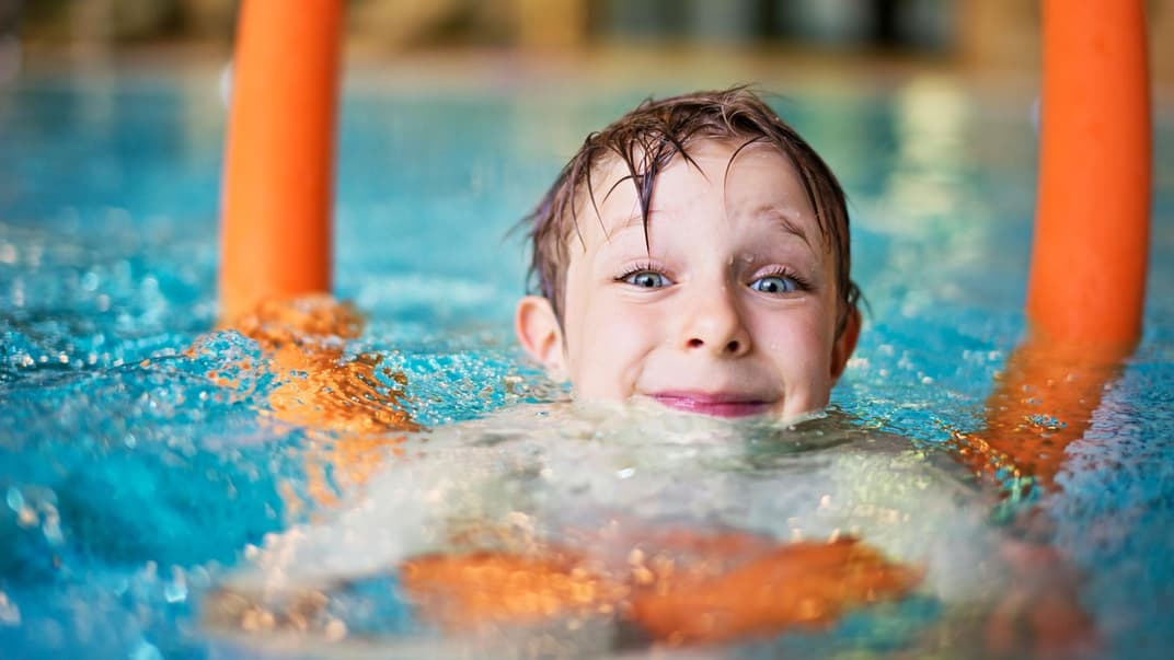 Kind mit Schwimmnudel im Wasser.