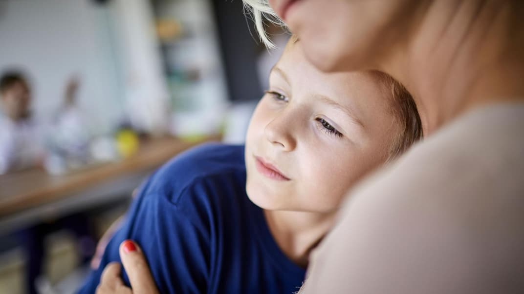 Parentifizierte Kinder ziehen sich manchmal im sozialen Umfeld zurück. Jüngere Kinder klagen mitunter über Bauchschmerzen oder Kopfweh. Ernster Sohn kuschelt mit Mutter.