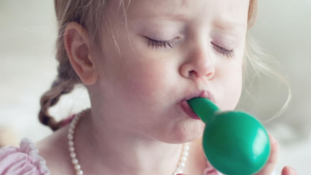 Mädchen pustet einen Luftballon auf.