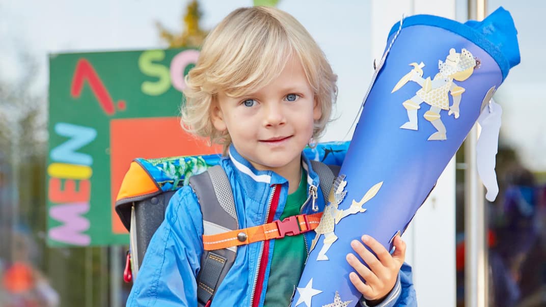 Ein kleiner Junge hat seinen Schulranzen auf und hält stolz seine Schultüte fest.