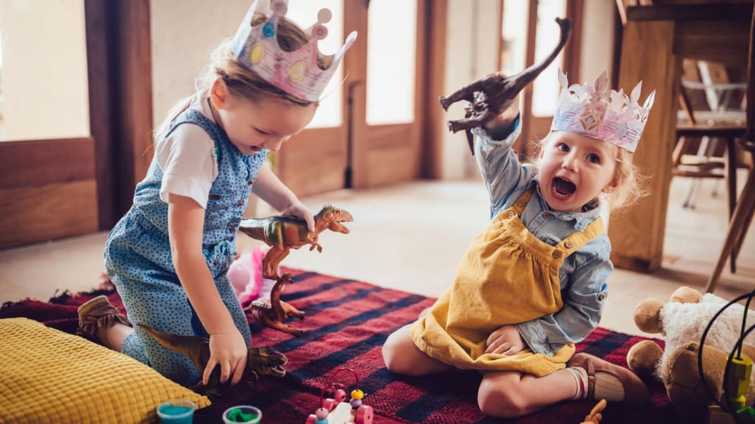 Zwei kleine Kinder spielen mit Dino-Figuren.