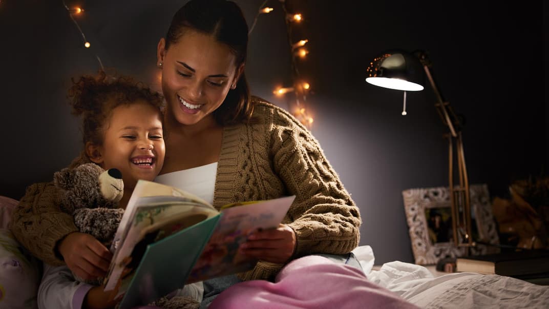 Mutter und Kind lachen beim abendlichen Vorlesen.