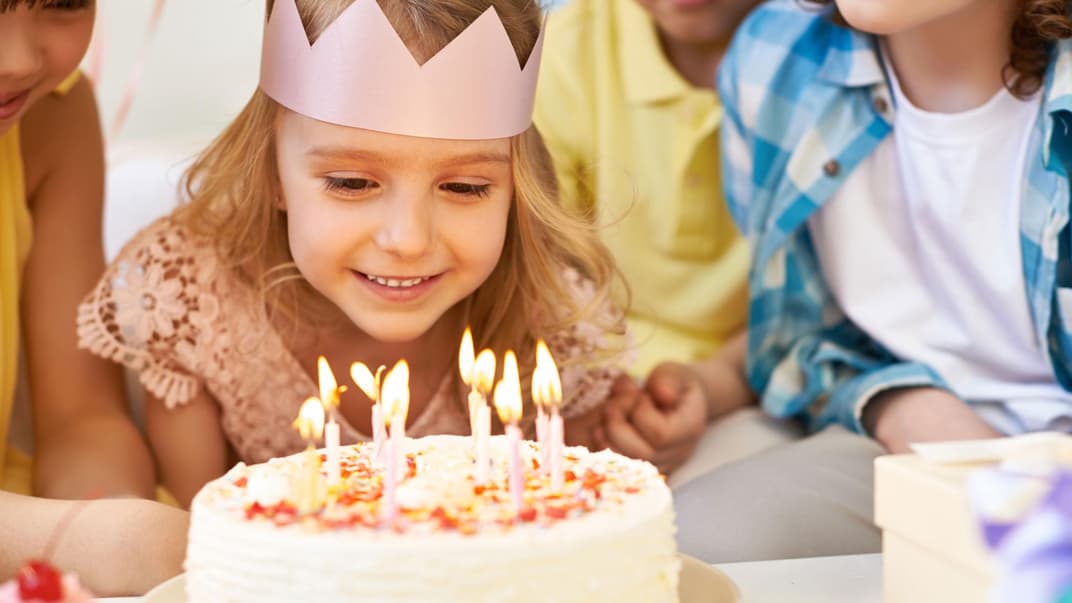 Ein Mädchen bläst die Kerzen auf ihrem Geburtstagskuchen aus. 