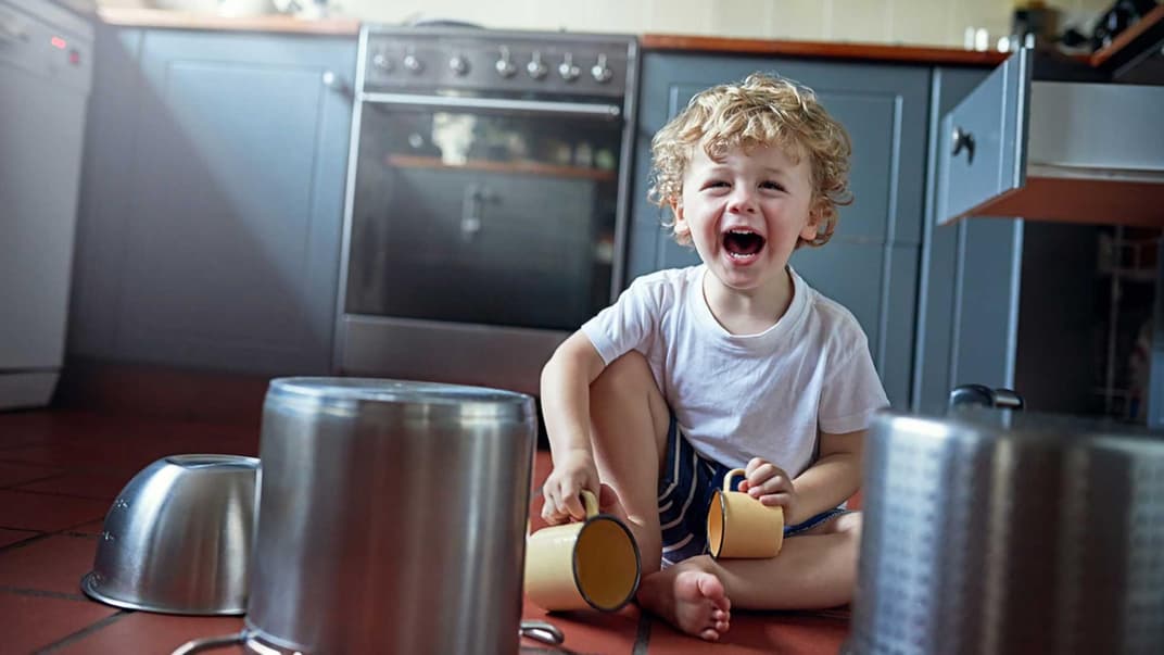 Kleinkind spielt fröhlich in der Küche mit Geschirr und Töpfen