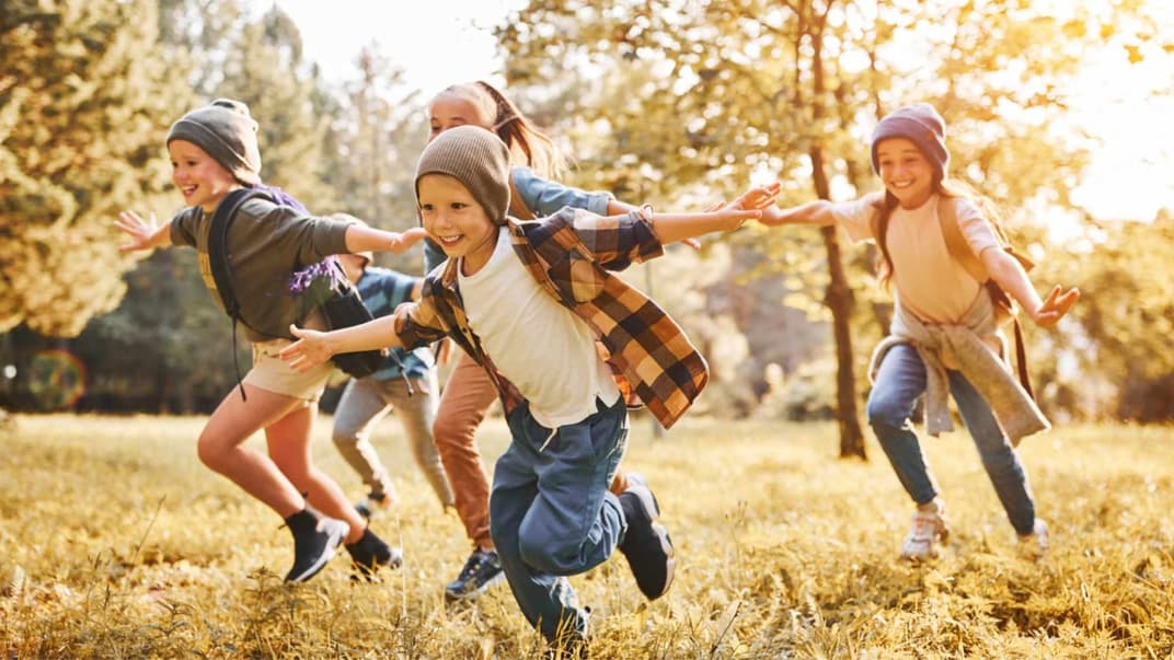 Kinder laufen fröhlich über eine herbstliche Wiese.