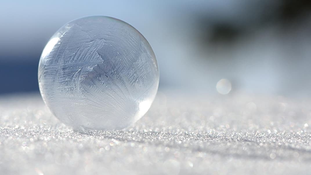 Eine gefrorene Seifenblase liegt auf einer Eisfläche.
