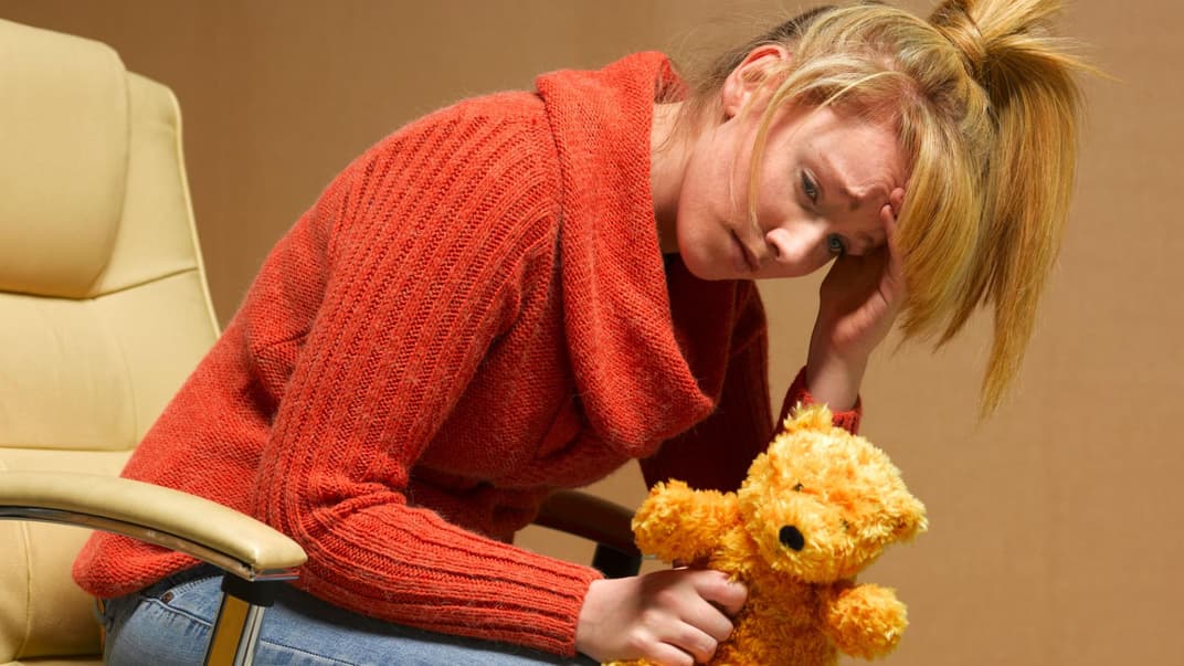 Erschöpfte, mutlose Frau mit Teddy in der Hand.