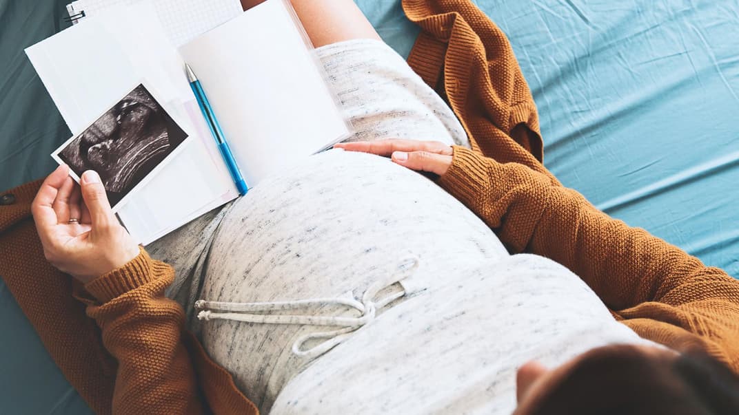 Schwangere schaut sich Mutterpass und Ultraschallbild an.