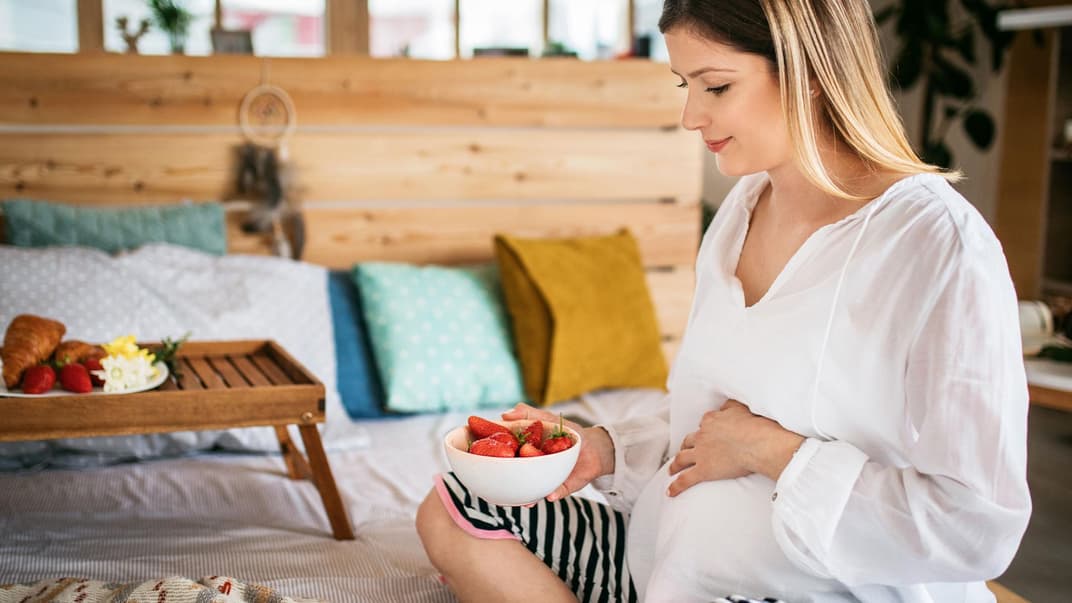 Schwangere Frau mit einer Schale Erdbeeren in der Hand Schwangere Frau mit einer Schale Erdbeeren in der Hand