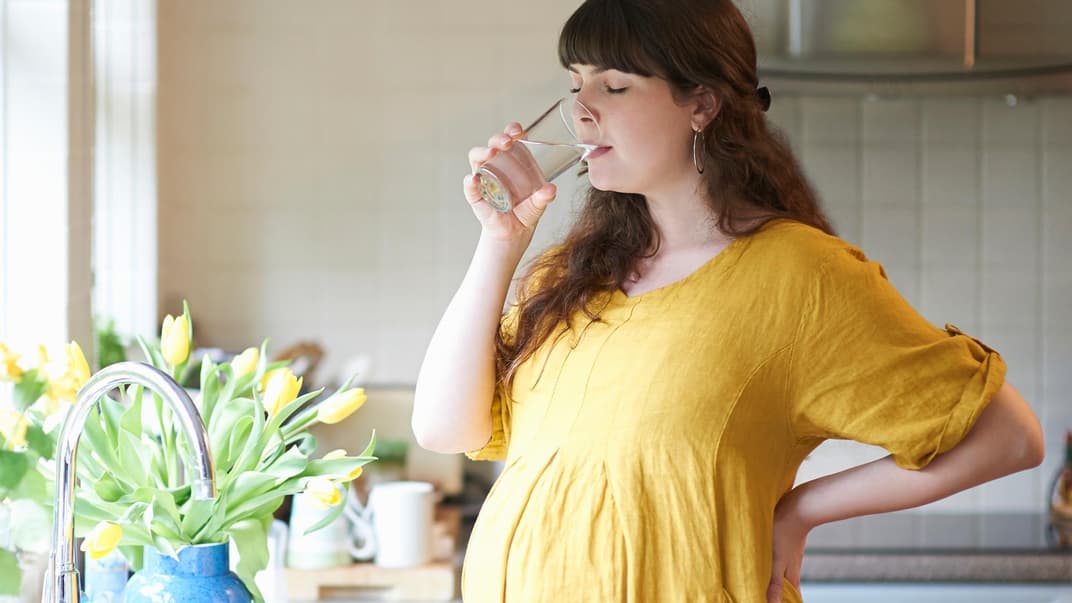Schwangere trinkt ein Glas Wasser.