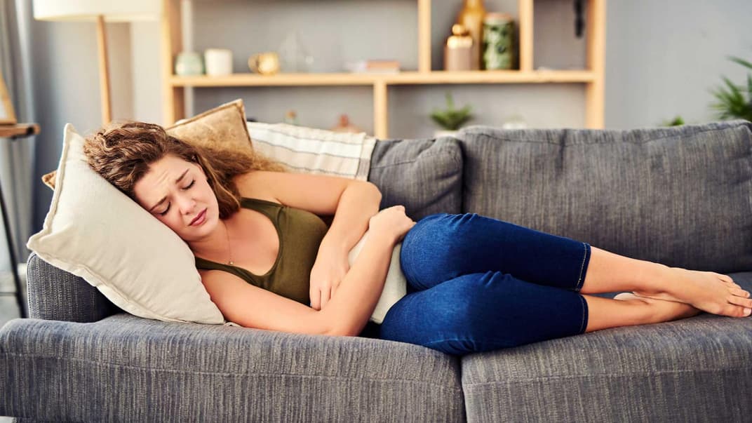 Frau liegt mit Bauchschmerzen auf dem Sofa.