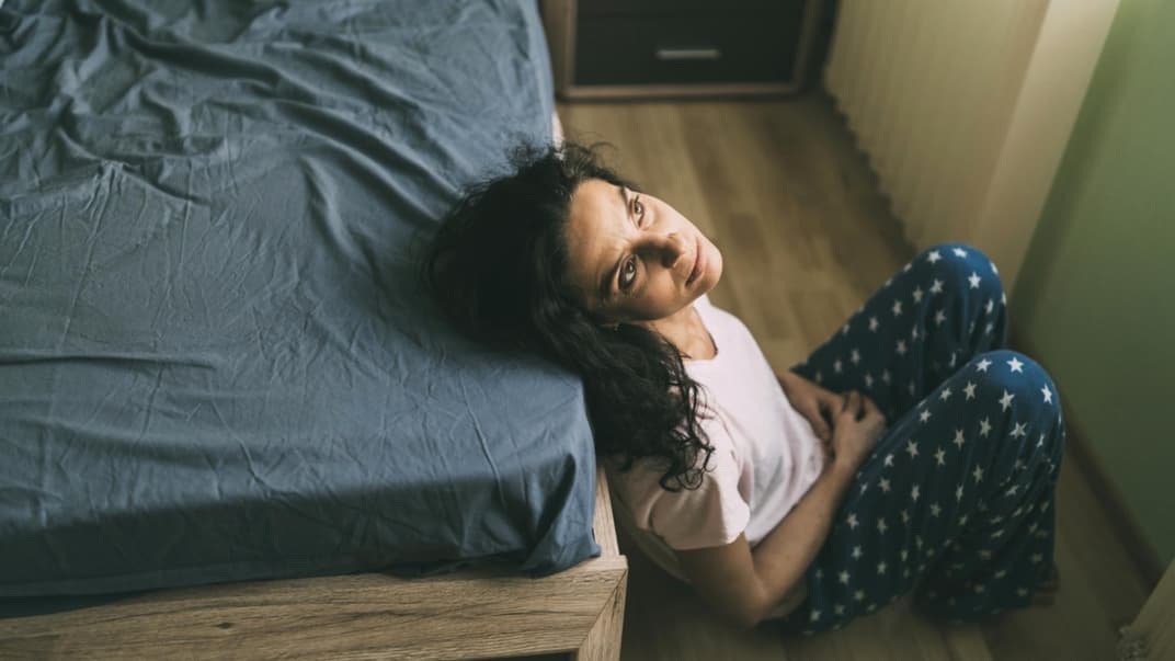 Frau sitzt vorm Bett und starrt an die Decke.