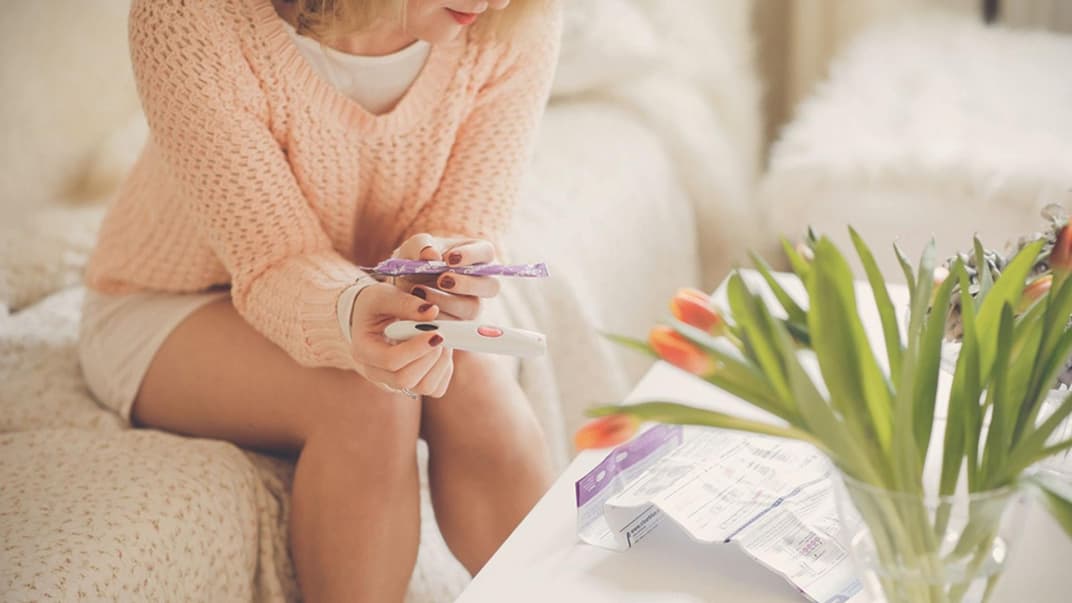 Frau sitzt vor Blumenstrauß mit Ovulationstest in der Hand.