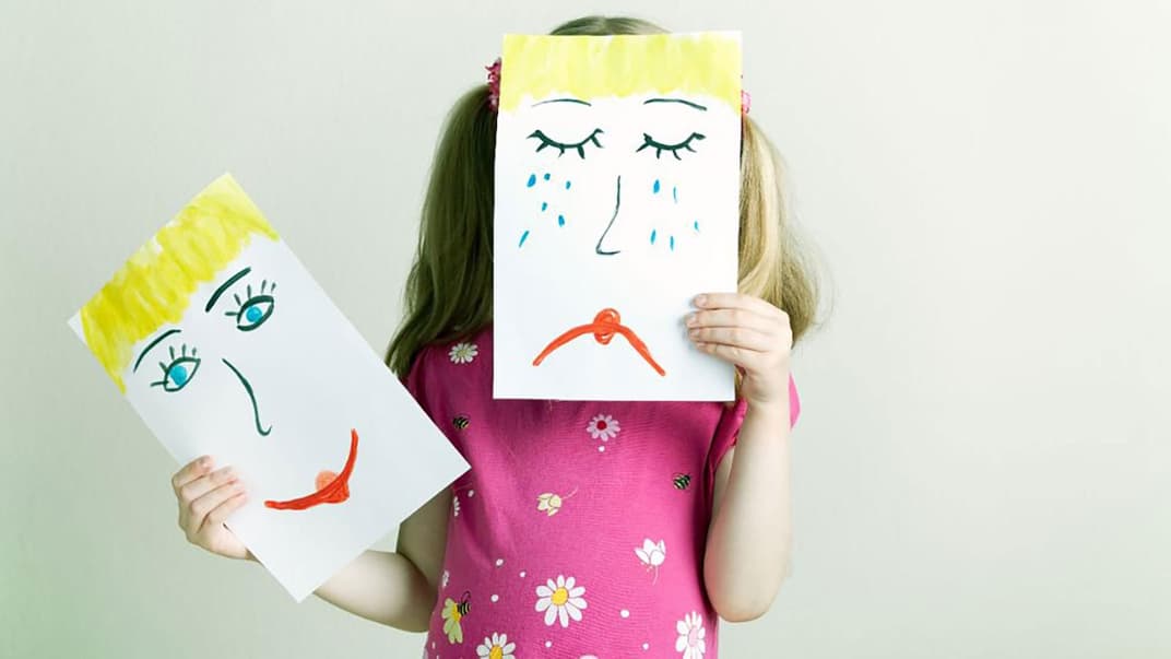 Gefühle zeigen: Kind hält gemaltes, trauriges Gesicht vor ihr eigenes.