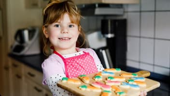 Ein kleines Mädchen hält ein Küchenbrett mit Osterkeksen.