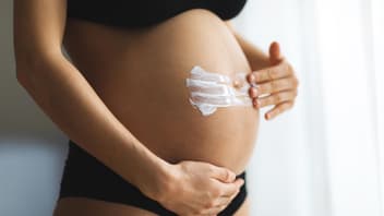 Eine Frau cremt ihren Babybauch ein.