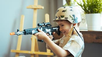 Kleiner Junge mit Tarn-Helm und Spielzeugwaffe