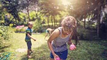 Zwei Kinder bewerfen sich im Garten mit Wasserbomben.